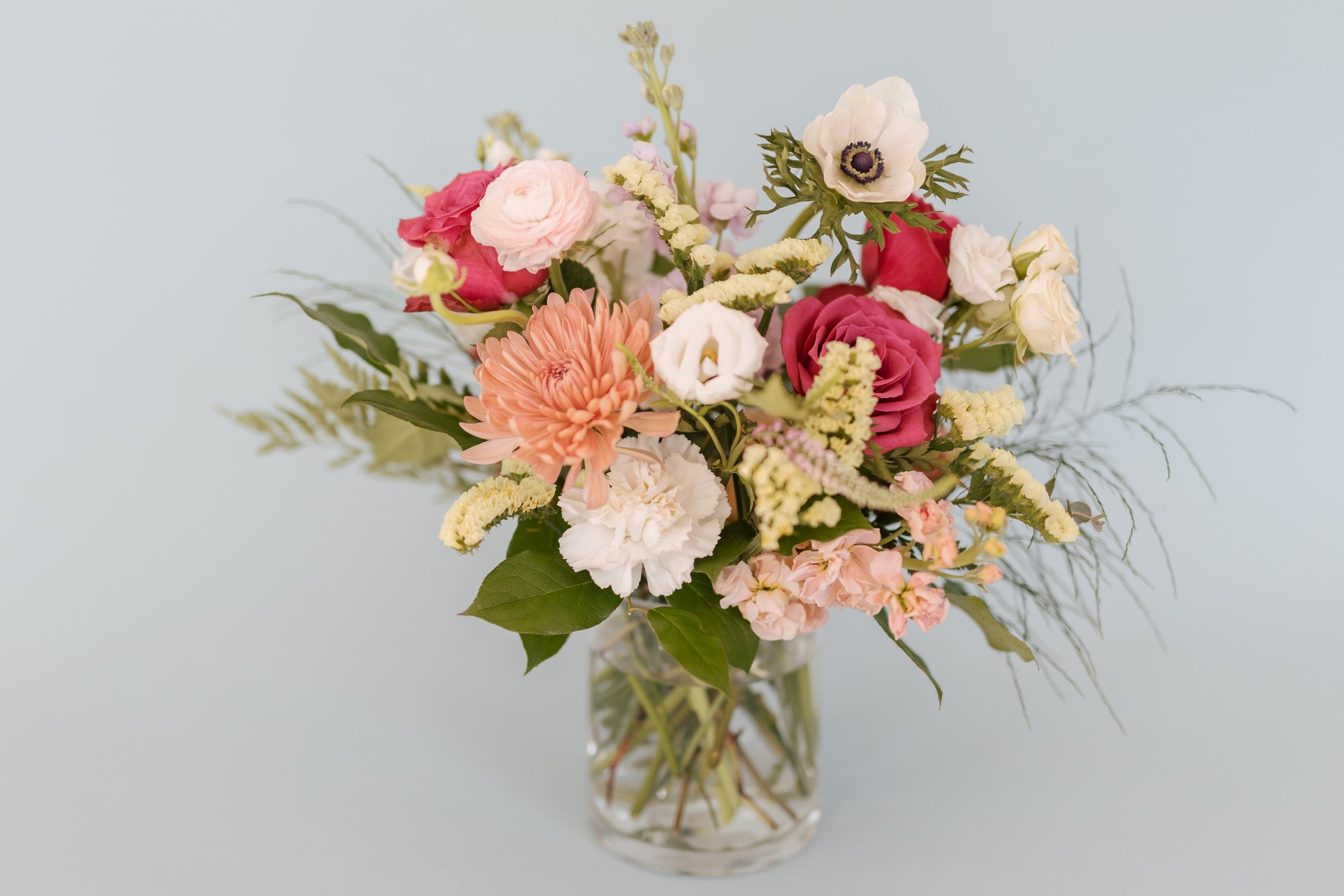 A vase arrangement of fresh flowers featuring a variety of colors and types, placed against a neutral background.