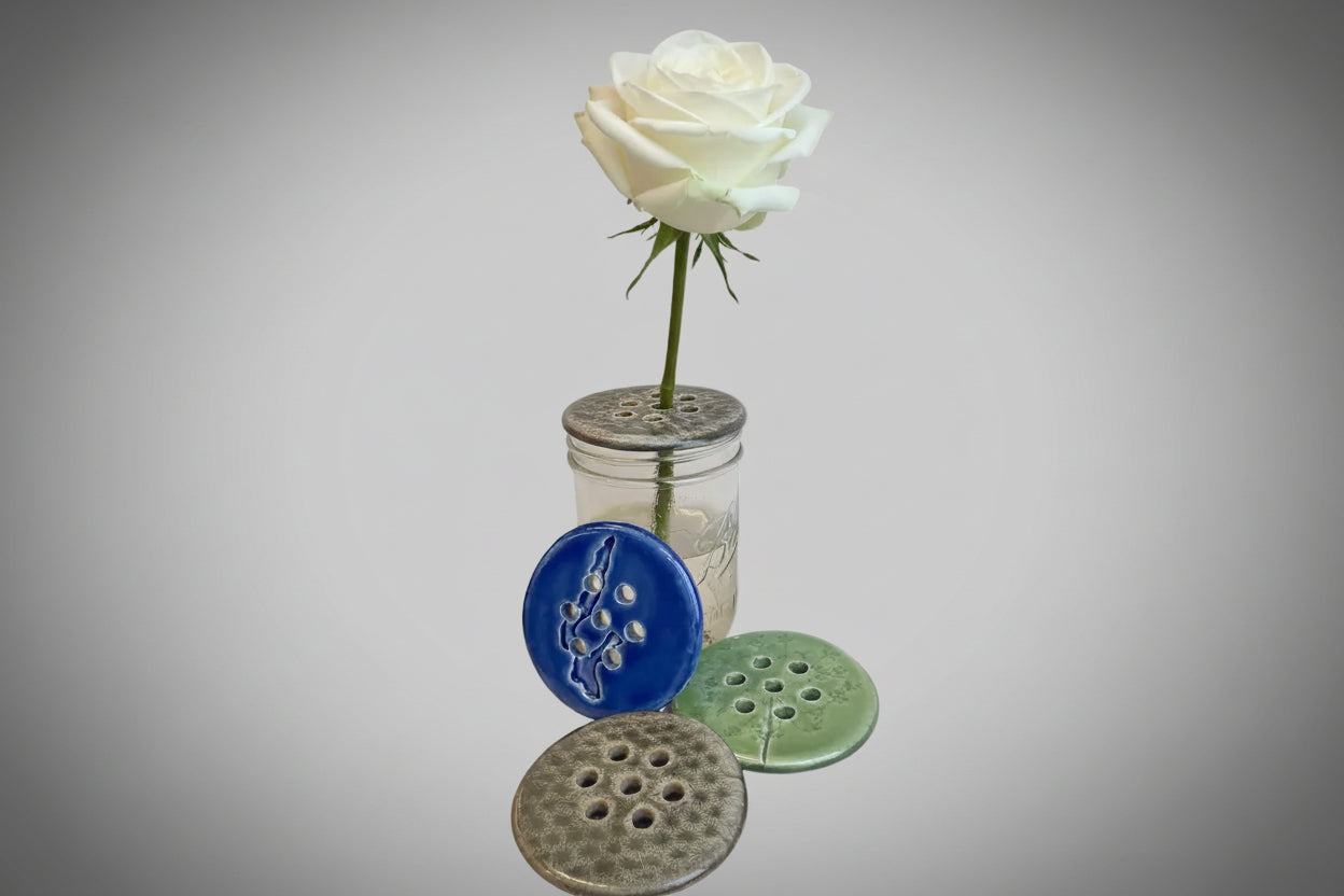 A collection of ceramic dishes in blue, green, and brown colors, displayed in front of a clear vase with a rose.