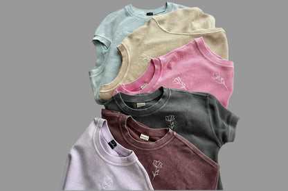 A collection of crew neck sweatshirts laid out on a surface, with colors including blue, pink, gray, and purple, and floral patterns on them.