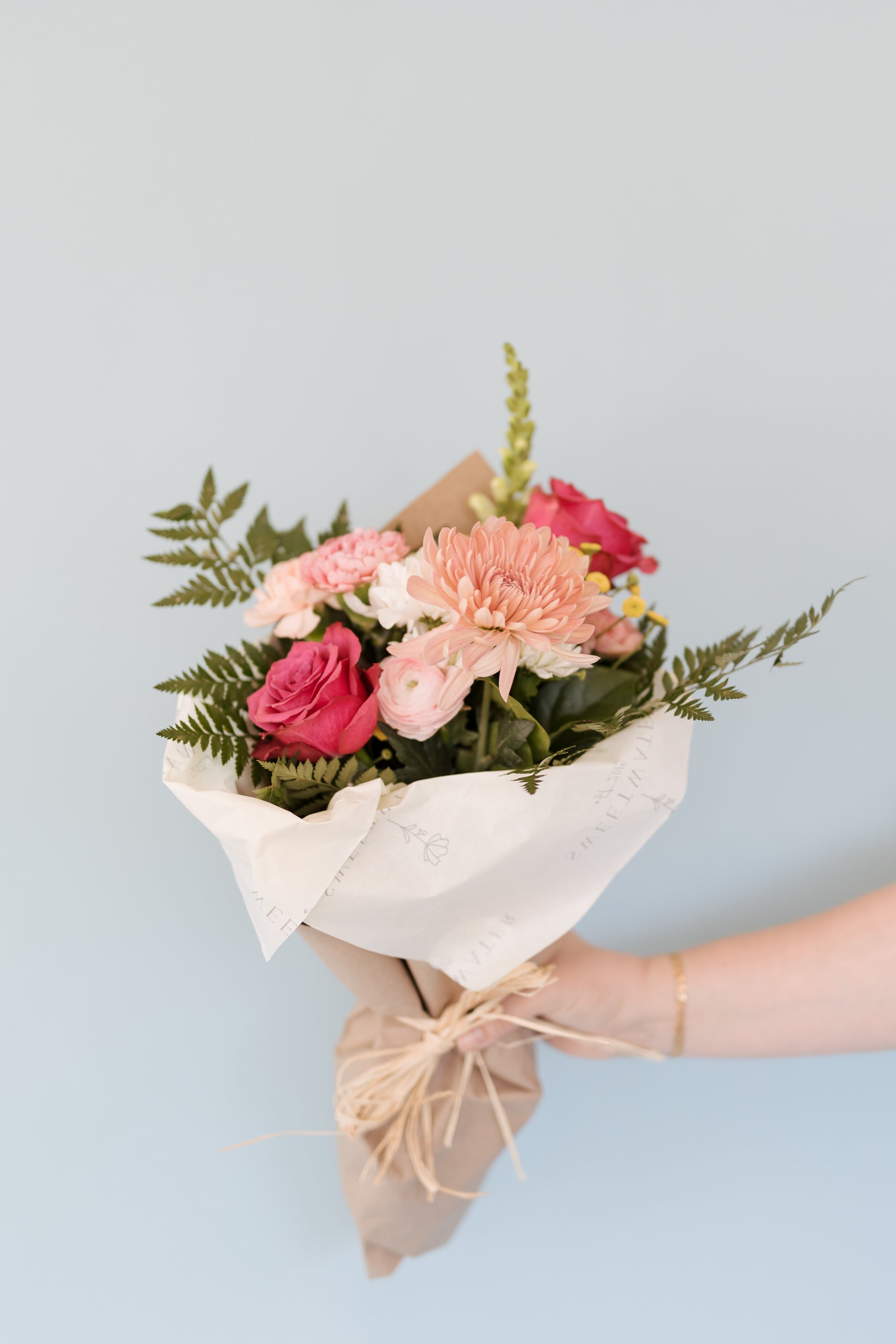 A wrapped bouquet of pink and red flowers with green foliage, tied with a ribbon.