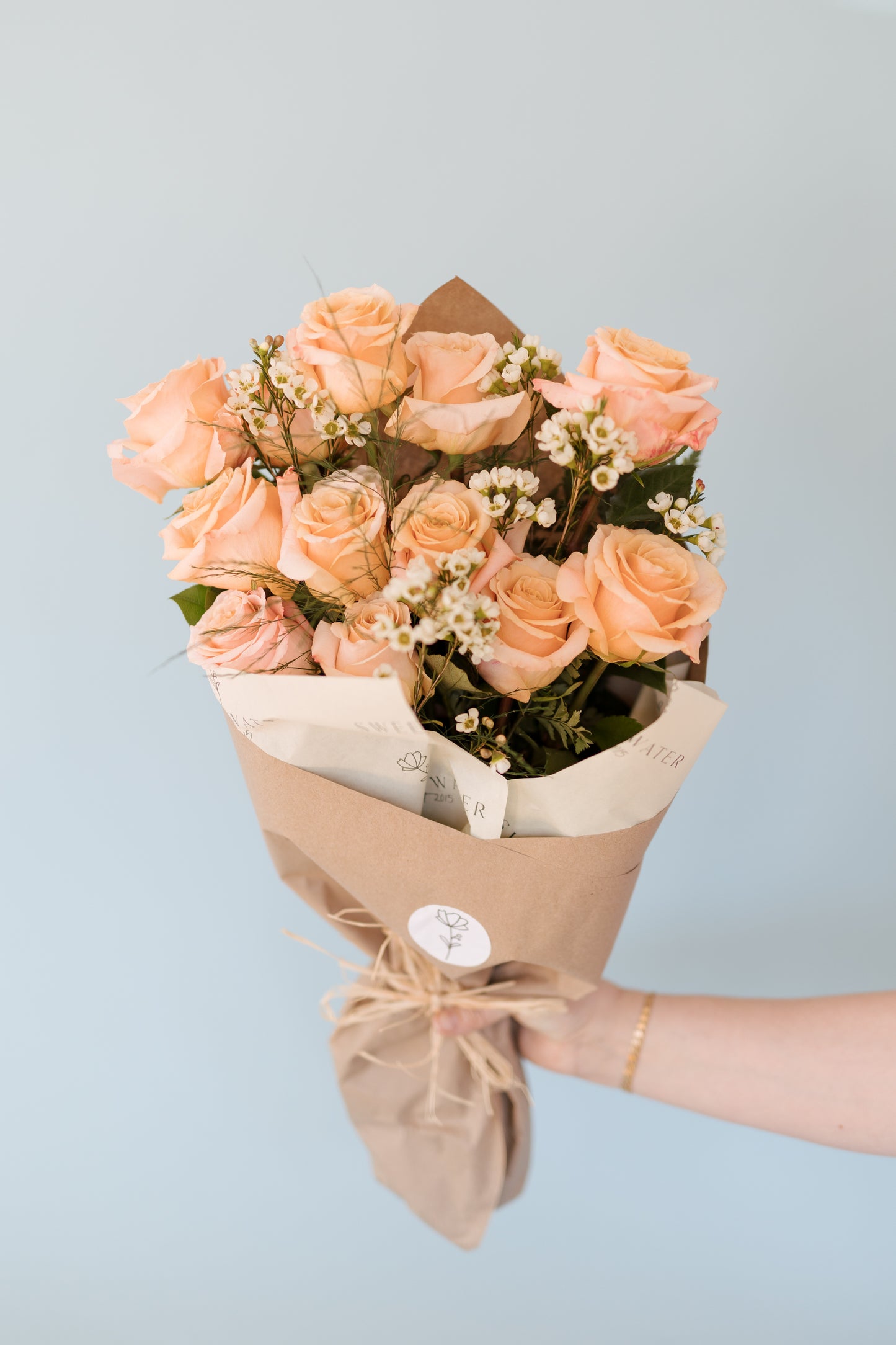 A bouquet of pink and white roses wrapped in brown paper with a blue background.